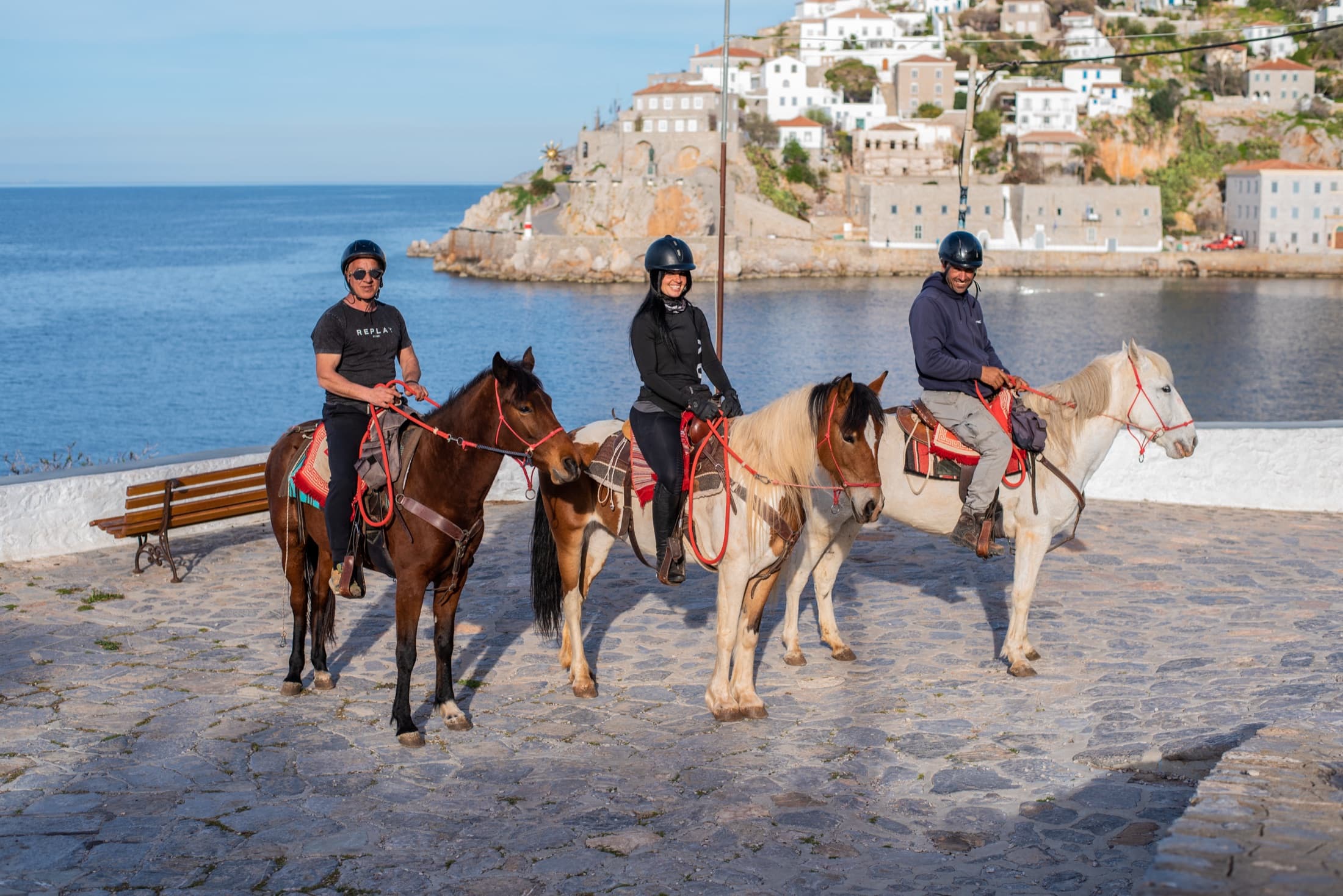 Riders on horseback on the cobbled waterfront of Hydra harbour, with the whitewashed town and Aegean Sea behind them